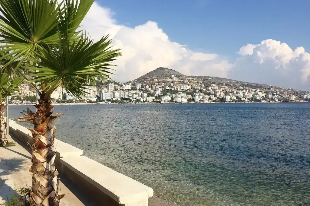 Retraités sur une terrasse face à la mer Ionienne en Albanie, avec un café à la main et les montagnes en arrière-plan
